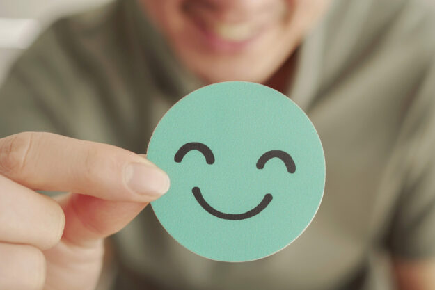 Hand holding green happy smile face paper cut, good feedback rat value for money assurance